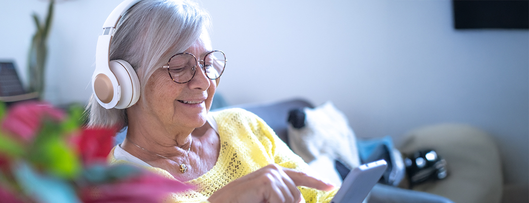 Image of senior woman wearing headphones and listening to audio on her smartphone